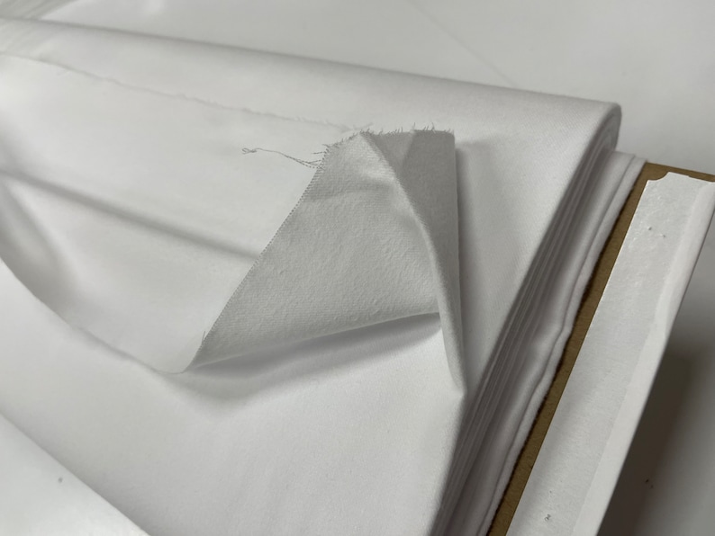 Op de afbeelding: Witte stof gevouwen in een stapel, wat de gladde textuur van het materiaal laat zien.