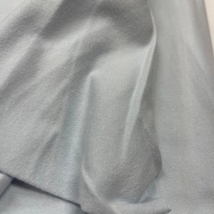 May include: A close-up of a light blue fabric with a smooth, soft texture. The fabric is folded and draped, showing its subtle sheen.