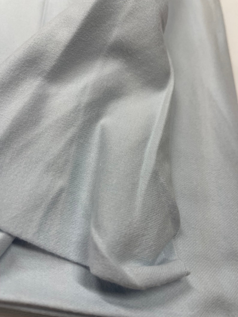 May include: A close-up of a light blue fabric with a smooth, soft texture. The fabric is folded and draped, showing its subtle sheen.