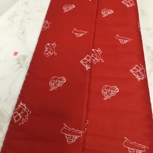 May include: Red fabric with a white repeating pattern of small cars. The fabric is folded in half.