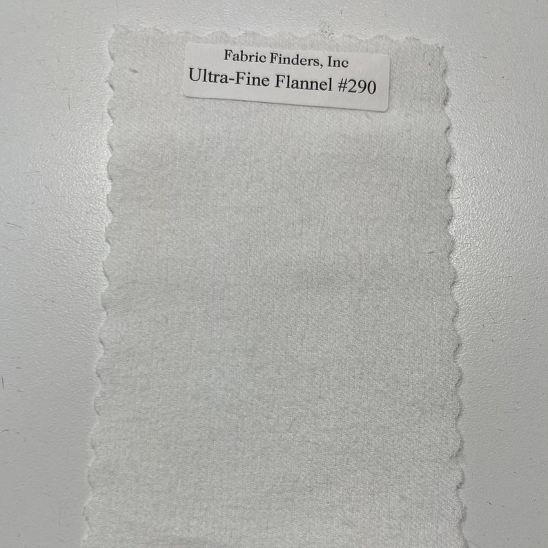 Op de afbeelding: Witte stofstaal met de tekst "Fabric Finders, Inc. Ultra-Fine Flannel #290" gedrukt op een label.