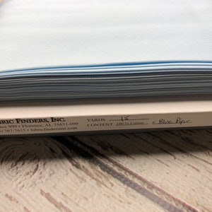 May include: A roll of light blue pique fabric, 100% cotton, with a label that reads "FABRIC FINDERS, INC." and "YARDS 15 CONTENT 100% Cotton # Blue Pique".