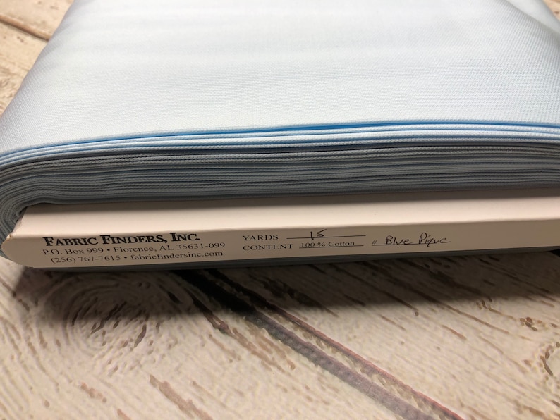 May include: A roll of light blue pique fabric, 100% cotton, with a label that reads "FABRIC FINDERS, INC." and "YARDS 15 CONTENT 100% Cotton # Blue Pique".
