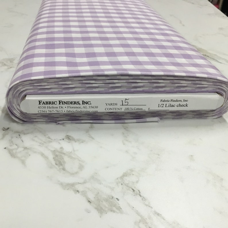 May include: A roll of 15 yards of 100% cotton fabric with a white and lilac gingham pattern. The label reads "Fabric Finders, Inc. 1/2 Lilac check".