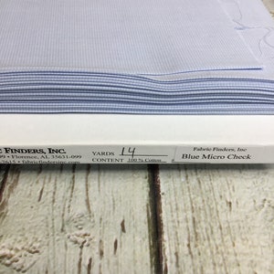 May include: A stack of light blue micro-check fabric. The fabric is 100% cotton and is labeled as 14 yards. The label also includes the name "Fabric Finders, Inc."