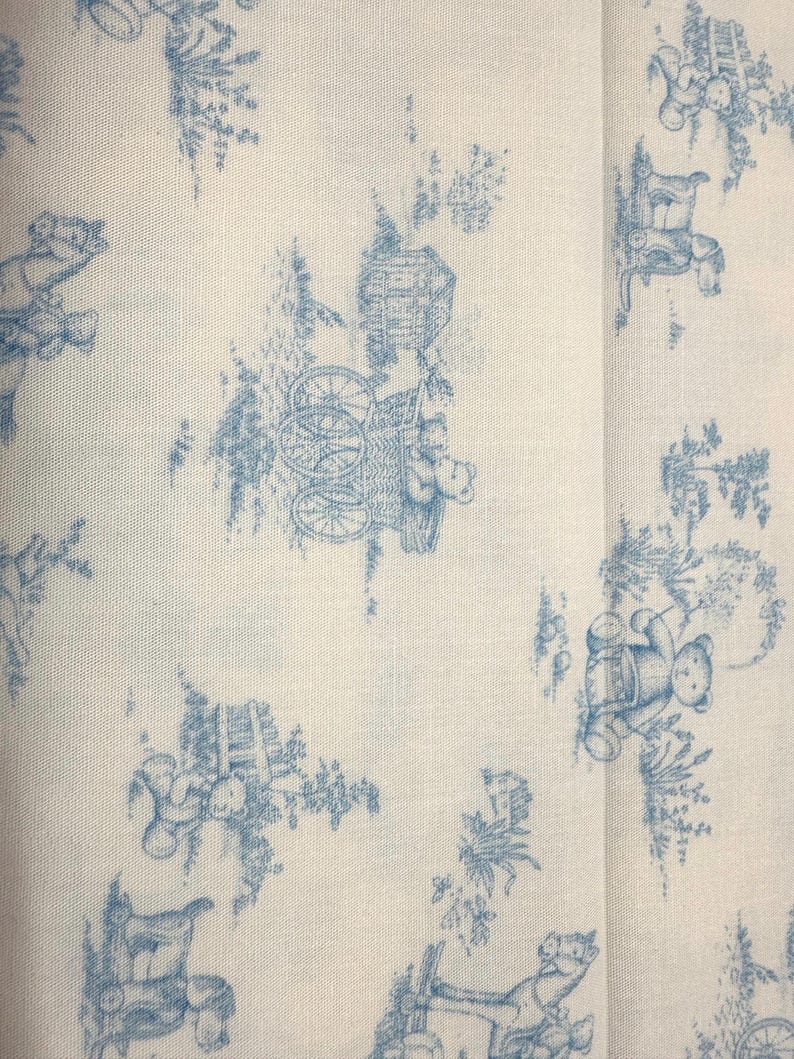 May include: Off-white fabric with a repeating blue toile pattern. The design features teddy bears, carriages, and floral elements. The fabric has a classic, vintage aesthetic, suitable for various craft projects.