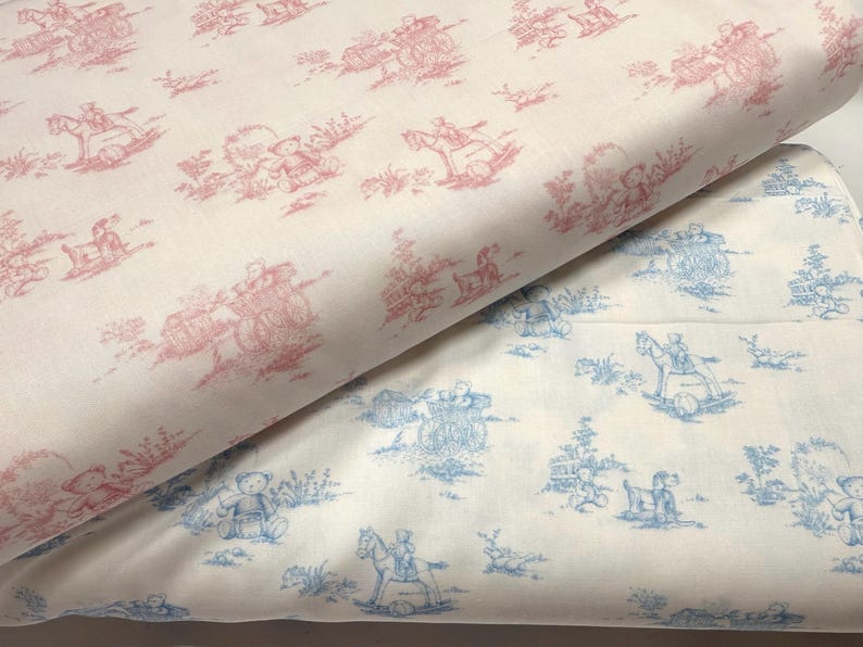 May include: Two rolls of fabric with a toile pattern. One roll features a red and white design with images of teddy bears, horse-drawn carriages, and children. The other roll has a blue and white design with similar imagery.