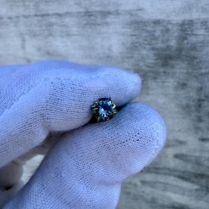 May include: A small, round, blue gemstone set in a silver bezel.