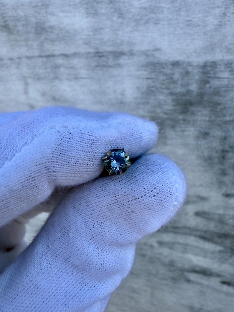 May include: A small, round, blue gemstone set in a silver bezel.
