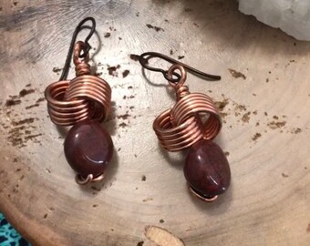 May include: A pair of copper wire earrings with brown stone beads. The earrings are in the shape of a knot.