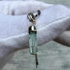 May include: A silver pendant necklace with a light blue crystal gemstone. The gemstone is a vertical, rectangular shape with visible facets. The pendant hangs from a delicate silver chain. The necklace is displayed against a white background.