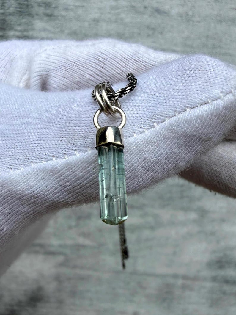 May include: A silver pendant necklace with a light blue crystal gemstone. The gemstone is a vertical, rectangular shape with visible facets. The pendant hangs from a delicate silver chain. The necklace is displayed against a white background.