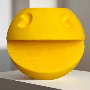 Puede incluir: Una escultura de cerámica de color amarillo brillante con forma de personaje de videojuego Pac-Man. La escultura está hecha de dos piezas, una superior y una inferior, que encajan entre sí.