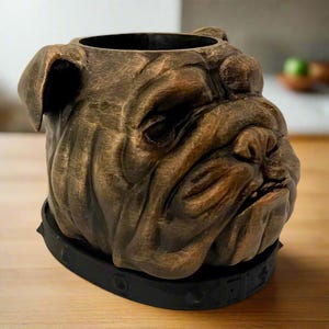 Könnte beinhalten: Ein bronzener Bulldoggenkopf-Pflanztopf mit einem schwarzen Halsband. Der Topf hat eine strukturierte Oberfläche und ein realistisches Design.