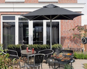 May include: A black patio umbrella provides shade over a black metal patio table and chairs. A black charcoal grill with a variety of food cooking on it is in the foreground.