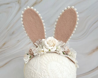 May include: A white headband with a lace trim and pearl accents. The headband is decorated with a white flower and two brown felt bunny ears with pearl trim.