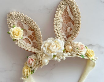 May include: A white headband with lace bunny ears decorated with white and yellow flowers and pearls.