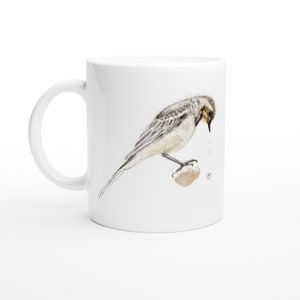 Op de afbeelding: Witte keramische mok met een aquarel-illustratie van een kleine vogel die op een rots zit. De vogel is grijs en wit met een gele borst.