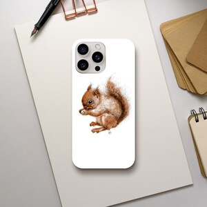 Puede incluir: Una funda de teléfono blanca con una ilustración de acuarela de una ardilla marrón sosteniendo una nuez. La funda del teléfono tiene un recorte para el objetivo de la cámara.