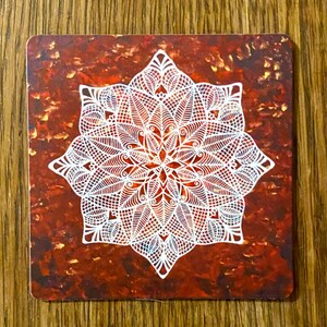 May include: A white mandala design with intricate details on a red and gold background.
