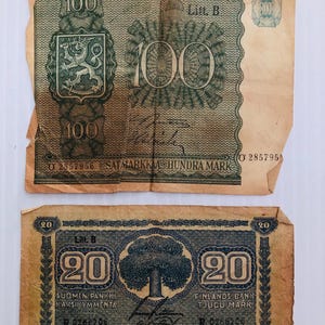 May include: Two vintage Finnish banknotes, one a 100 mark note with a lion crest and the other a 20 mark note with a tree design. Both notes are faded and worn, with the text "SUOMEN PANKKI FINLANDS BANK" visible on both.