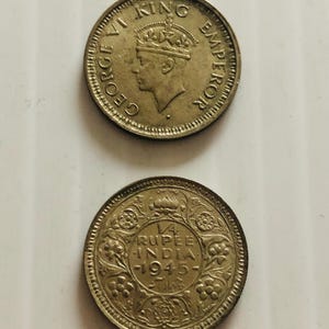 May include: A gold-colored coin with the inscription "GEORGE VI KING EMPEROR" on one side and "1/4 RUPEE INDIA 1945" on the other side.