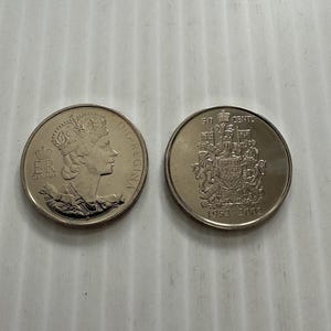 Op de afbeelding: Twee Canadese 50-centmunten. Eén munt toont een profiel van koningin Elizabeth II en de inscriptie "ELIZABETH II D. G. REGINA CANADA". De andere munt toont een wapenschild en de tekst "50 CENTS 1952-2002". Beide munten zijn zilverkleurig.