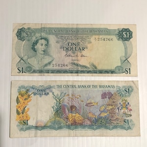 Könnte beinhalten: Zwei ein Dollar-Scheine der Bahamas. Der obere Schein zeigt ein Porträt von Königin Elisabeth II. und den Text "THE CENTRAL BANK OF THE BAHAMAS". Der untere Schein zeigt eine farbenfrohe Unterwasserszene mit Fischen und Korallen und den Text "THE CENTRAL BANK OF THE BAHAMAS".