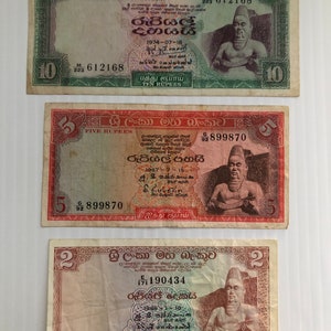 May include: Three Sri Lankan banknotes, one ten rupee note, one five rupee note, and one two rupee note. The notes feature a portrait of a man in a traditional headdress and a lion.