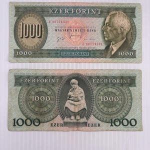 May include: Two Hungarian 1000 Forint banknotes. The top bill features a portrait of a man and the text "EZER FORINT". The bottom bill shows a woman holding a baby. Both bills have the number "1000" prominently displayed.