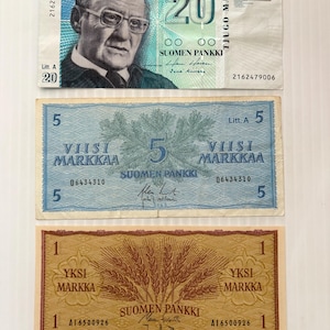 May include: Three vintage Finnish banknotes. The top note is a 20 Markkaa bill with a portrait of a man wearing glasses. The middle note is a 5 Markkaa bill with a pine branch design. The bottom note is a 1 Markka bill with a wheat design.