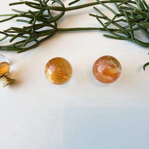 May include: Three round glass cabinet knobs with gold flecks and a clear background. The knobs are arranged in a row on a white surface.