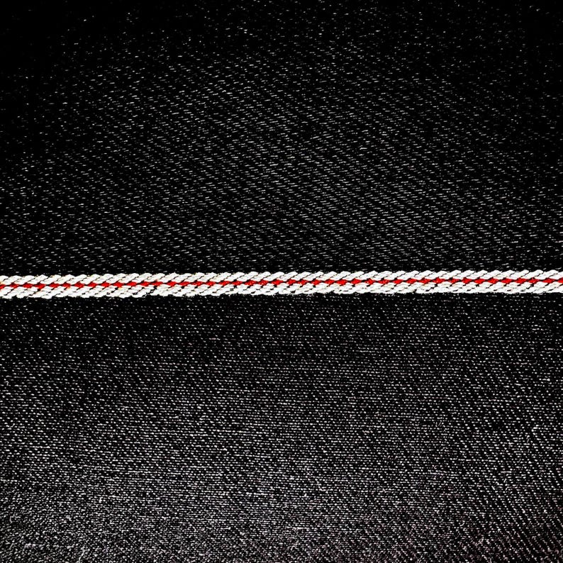 May include: Black denim fabric with a single red and white stitched line across the middle.