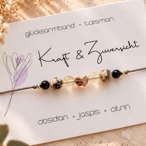 Könnte beinhalten: Ein Armband auf einer weißen Karte mit dem Text glücksarmband talisman Kraft & Zuversicht obsidian jaspis citrin. Das Armband besteht aus schwarzen Perlen, gesprenkelten Jaspisperlen, gelben Citrinperlen und einem roségoldenen Herz in der Mitte.