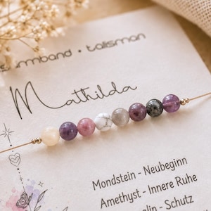 Peut inclure: Un bracelet délicat composé d'une rangée de huit perles en pierres semi-précieuses lisses et multicolores dans des tons crème, violet, rose, blanc, gris et vert foncé, montées sur un fil doré fin, présenté sur une carte avec le nom Mathilda.
