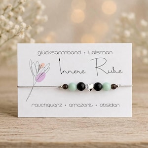 Könnte beinhalten: Ein zartes Armband mit silbernem Band, mit schwarzen, mintgrünen und braunen Perlen sowie einem kleinen silbernen Herzanhänger. Das Armband wird auf einer weißen Karte mit den Worten "Innere Ruhe" und "rauchquarz • amazonit • obsidian" präsentiert.