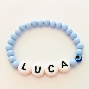 Könnte beinhalten: Hellblaues Perlenarmband mit einem weißen bösen Blick-Anhänger und dem Namen "LUCA" in weißen Perlen.