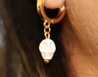 May include: Gold hoop earrings with a white skull charm dangling from a gold chain.