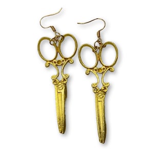 May include: A pair of gold-coloured scissor earrings. The earrings are in the shape of a pair of scissors with ornate details.