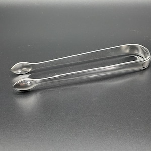 May include: Silver sugar tongs with rounded ends. The tongs are made of polished metal and have a simple design.