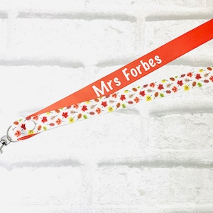 May include: A red and white lanyard with a fall leaf pattern. The lanyard has the text "Mrs. Forbes" printed on the red side.