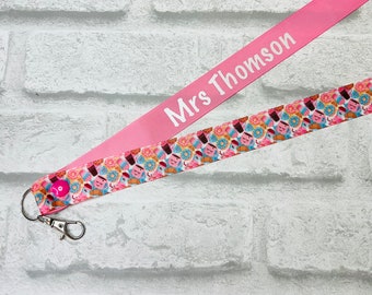 May include: Pink lanyard with a white text that says "Mrs. Thomson" and a colorful pattern of donuts and other treats.