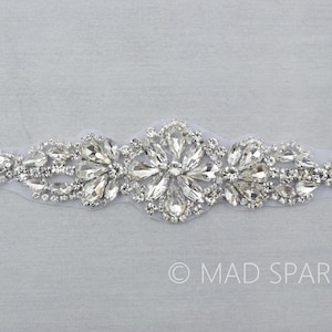 May include: A silver rhinestone applique with a floral design. The applique is on a clear mesh backing.