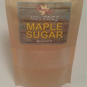 May include: A brown paper bag with a label that reads "100% Pure Maple Sugar" and "Net 8 oz (227 g)". The bag contains a light brown powder.