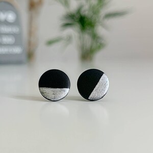 May include: A pair of round stud earrings in black and silver. Each earring features a silver accent on the lower half.