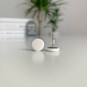 Op de afbeelding: Een paar witte ronde oorbel studs met zilveren pinnen.