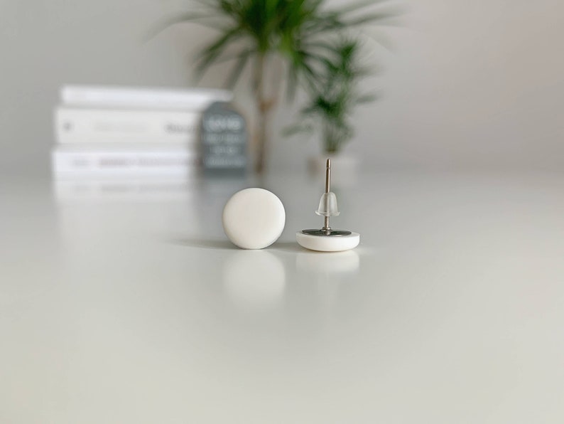 Op de afbeelding: Een paar witte ronde oorbel studs met zilveren pinnen.