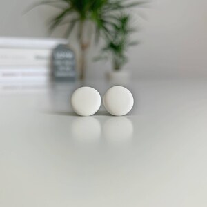 Op de afbeelding: Een paar witte ronde oorbel studs. De oorbellen zijn klein en eenvoudig en zouden een geweldige aanvulling zijn op elke sieradencollectie.