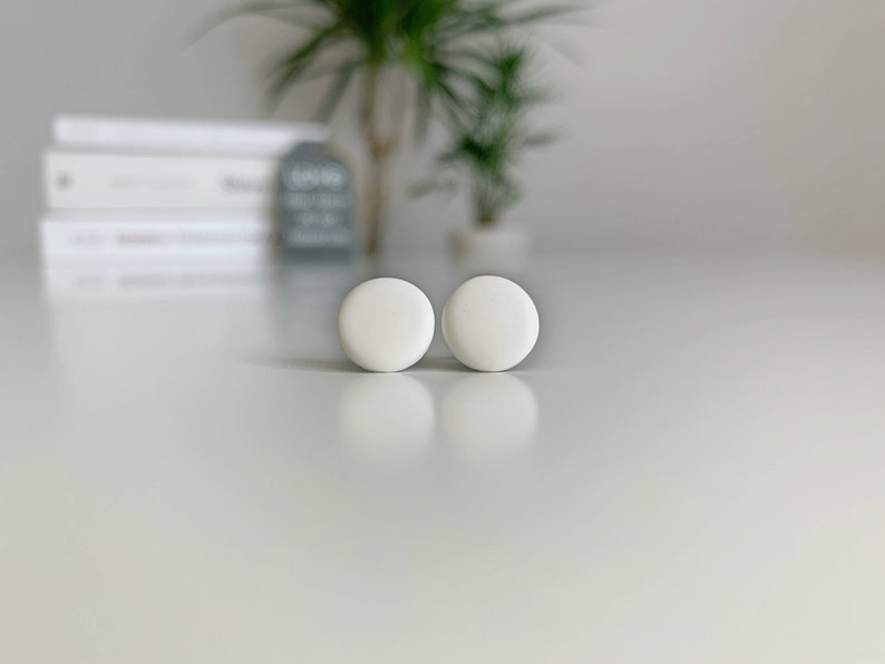 Op de afbeelding: Een paar witte ronde oorbel studs. De oorbellen zijn klein en eenvoudig en zouden een geweldige aanvulling zijn op elke sieradencollectie.