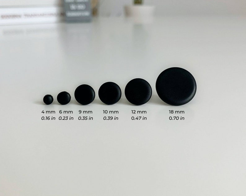 May include: A set of six black round buttons in various sizes, ranging from 4 mm to 18 mm. The buttons are arranged in order of size, with the smallest button on the left and the largest button on the right. The buttons are all made of the same material and have a smooth, matte finish.